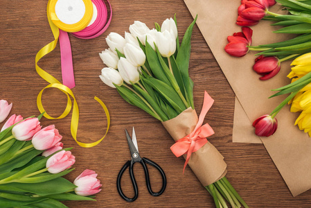 花艺花束郁金香丝带和手工纸在木制背景上的俯视图