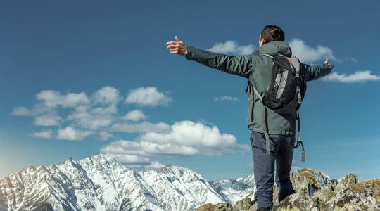 男性游客庆祝成功，在阳光明媚的日子里，他们张开双臂站在雪山的背景上。 激励和实现目标的概念