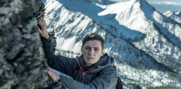 游客带着背包，在雪山的背景下，在岩石上爬行到山顶。 动机和目标实现的概念