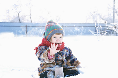 穿着冬衣的婴儿在户外摘下手套，打个招呼。可爱的孩子戴着帽子围巾和手套在雪地里