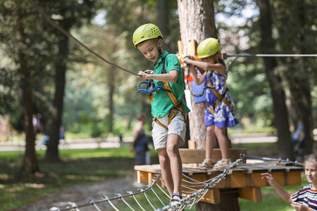 穿着防护装备和安全帽,在阳光明媚树木模糊的背景下,在索道上攀爬