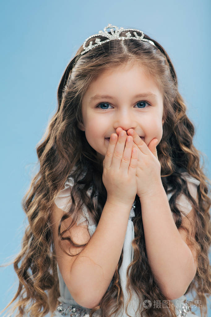 正面美丽微笑的形象,孩子双手放在嘴上,长发浓密,蓝色的眼睛戴着皇冠