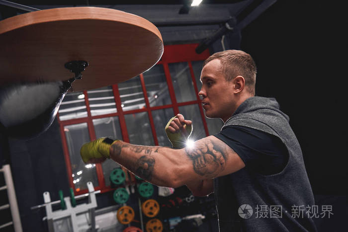 在拳击健身房训练拳击技能时, 年轻拳击手用绿手绷带打打拳速度包的侧