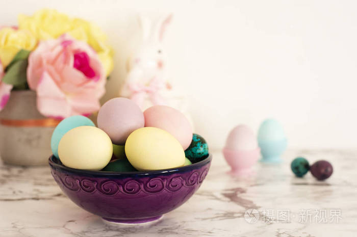 复活节彩蛋。 紫色碗，五颜六色的鸡蛋在哑光的颜色。 浅大理石背景