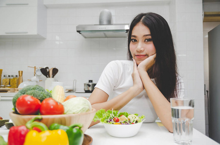 美丽的年轻亚洲女人苗条的身体穿着白衬衫节食和吃健康的食物新鲜蔬菜沙拉坐在厨房内部的家庭生活方式，良好的健康饮食，食物和饮料的概念