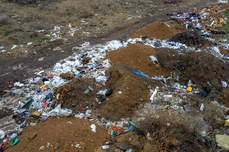 一大堆垃圾的鸟瞰图。 堆放在非法元素垃圾场或填埋场的垃圾，许多家庭垃圾塑料袋在房子前面。 垃圾填埋环境废物