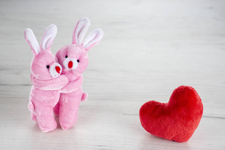 粉红色玩具兔子拥抱在红色毛绒心附近