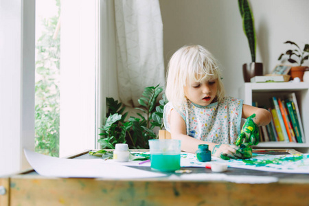可爱的小女孩在家玩绿色油漆靠近窗户