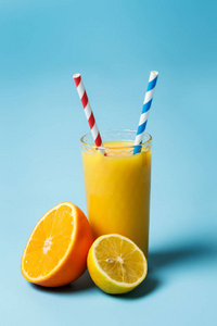 一杯新鲜的朱丝和两个纸管旁边的柠檬和一个橙色的蓝色背景与复制空间