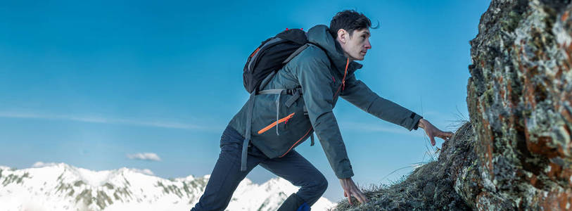 一个背包在岩石上爬行的人，在雪山的背景下爬到山顶。 动机和目标实现的概念