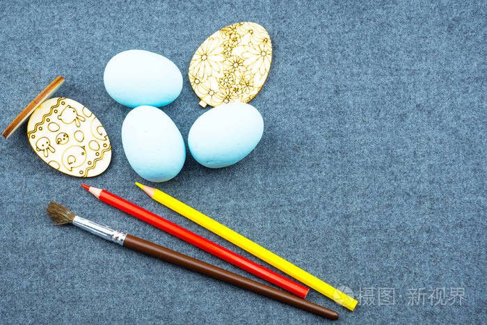 蓝色泡沫鸡蛋,木形鸡蛋,彩色铅笔,刷子. 背景织物灰色模糊.