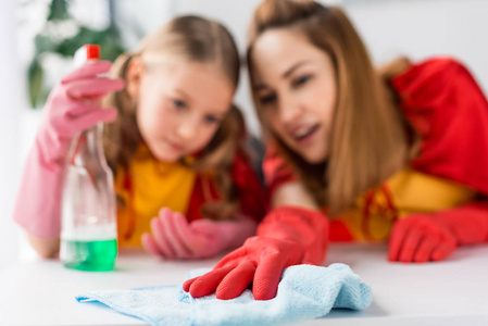 母亲和女儿在家里用红斗篷和橡胶手套除尘的选择性专注