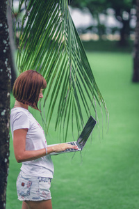 女性网上购物的概念。自由职业者妇女在绿色公园与现代笔记本电脑。巴厘岛