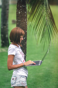 女性网上购物的概念。绿色公园里的女人配着现代化的笔记本电脑。巴厘岛