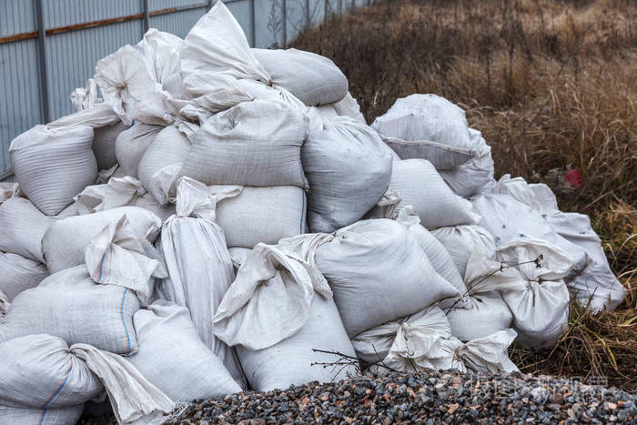 白色建筑垃圾麻袋被倾倒在正在施工的围栏附近的堆中。 污染概念。 垃圾填埋场垃圾场中的垃圾。 非法垃圾场回收