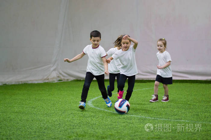 穿着白色t恤的孩子们在室内踢足球孩子们在球后在场上跑