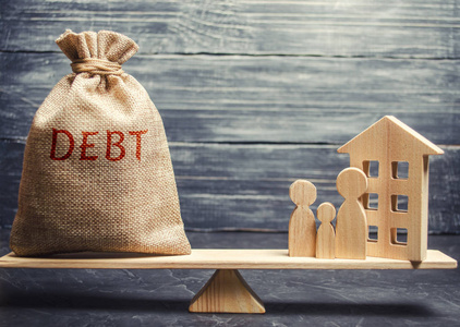 有债务这个词的钱袋和一个微型房子，上面有一个家庭。 偿还房地产债务。 还清抵押贷款。 买房子的风险。 赊购公寓
