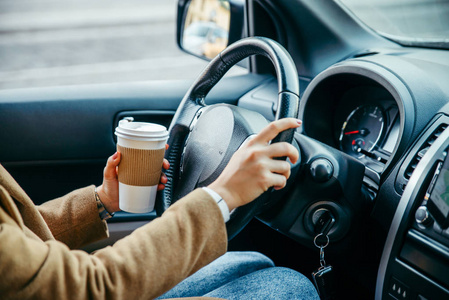 女人的手闭上。 开着车。 从里面看。 喝咖啡。 公路旅行