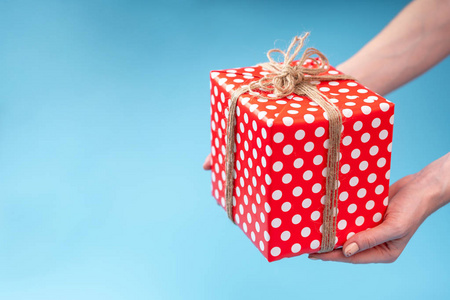 s hands holding gift box Packed in red polka dot paper on blue b