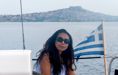 一个戴着墨镜的女人坐在挂着希腊国旗的帆船驾驶舱里，莱斯沃斯的莫利沃斯镇