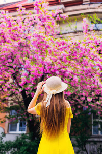 一个穿着帽子的女孩站在镜头前，手拿着一顶靠近建筑物和日本樱桃的帽子