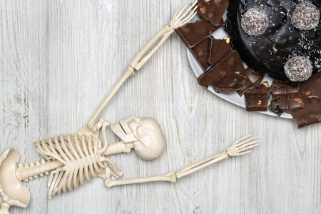 巧克力蛋糕和盘子上的切片，木桌上的骨架。 平躺着。 糖尿病死亡的概念。