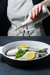 s hands watered Dorado fish with olive oil. Dark background, sid