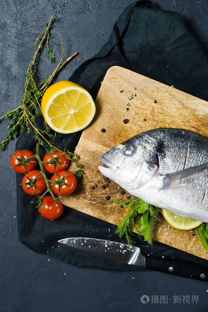 把多拉多鱼塞在木制砧板上配料迷迭香西红柿辣椒柠檬百里香胡椒盐深色