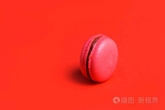 极简主义. 一个珊瑚或粉红色的法国马卡龙在红色背景特写拷贝空间