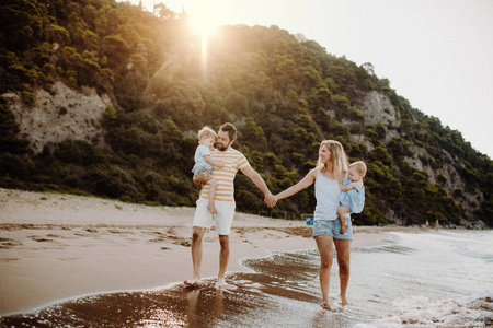 一个家庭带着两个幼儿在暑假日落时走在海滩上
