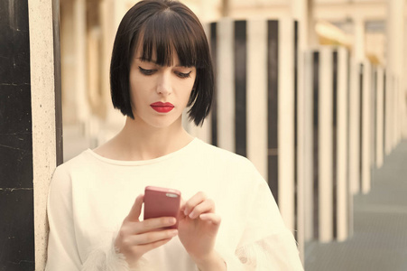 时尚模型与移动设备。法国巴黎, 在智能手机上使用红唇的女人。有黑发的女人拿着手机。美丽的女孩与的外观。现代生活新技术