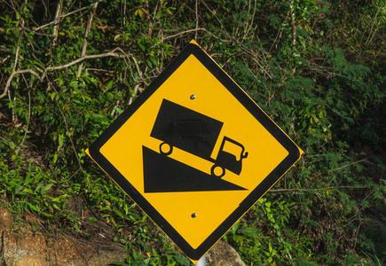 陡峭的路标，卡车沿着陡峭的斜坡行驶。 雨林背景。 黑色和黄色。