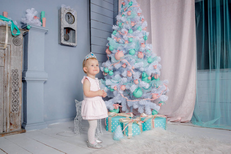 一个可爱的小欧洲金发公主的肖像，戴着一顶漂亮的皇冠，穿着一件漂亮的连衣裙，在一个装饰着圣诞主题的工作室里，玩具和圣诞树。