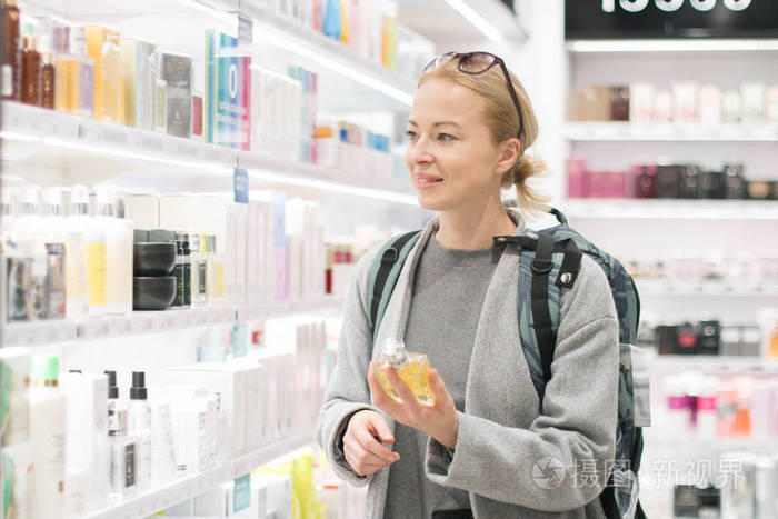 穿着旅行背包的金发年轻女性旅行者在机场免税店选择香水照片 正版商用图片18gp2o 摄图新视界