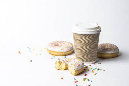 一个纸杯，有盖子咖啡或茶，新鲜美味的甜甜圈和甜的多色装饰糖果在白色的背景。 面包店概念新鲜糕点美味早餐快餐