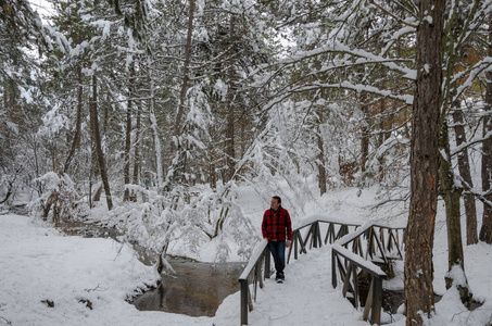 美妙的冬季景观。小溪和树木被雪覆盖着。衬衫的人在冬天的木桥上环顾四周。