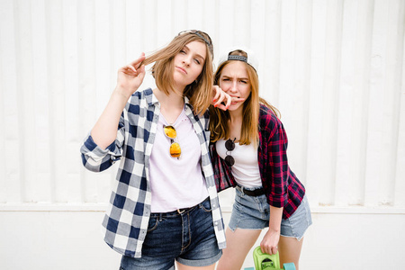 两个开朗有趣的女孩穿着格子衬衫, 在街上的墙壁上摆姿势