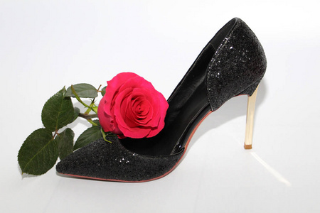 粉红色的玫瑰穿着女鞋。带高跟鞋的黑鞋。玫瑰在一只黑鞋旁边。