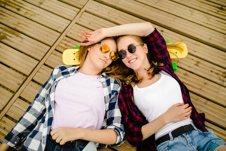 两个长板的时尚年轻城市女孩躺在街道的木地板上。朋友们在假期里一起度过快乐时光