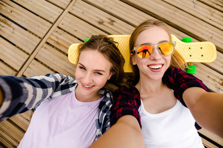 两个穿着嬉皮士服装的年轻女孩躺在木码头上做自拍
