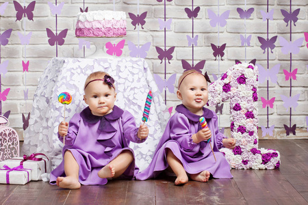 一岁的双胞胎生日。 可爱的双胞胎姐妹庆祝他们的1岁生日。 小双胞胎女孩坐在地板上吃糖果