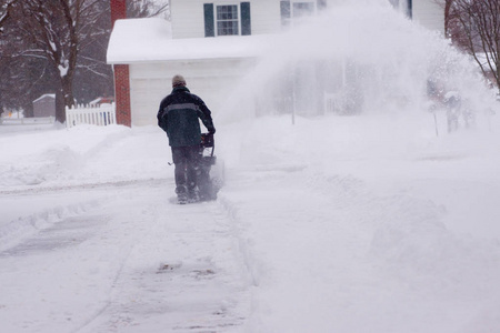 在暴风雪中，一个男人在他的车道上使用吹雪机