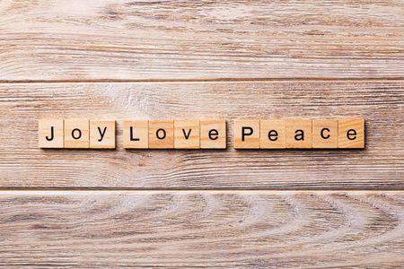 欢乐爱和平的词写在木块上。 欢乐爱和平文本在木桌上为您的设计概念。