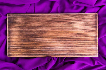 紫色紫罗兰餐巾布背景上的木切割板。 平躺着。 复制空间顶部视图。