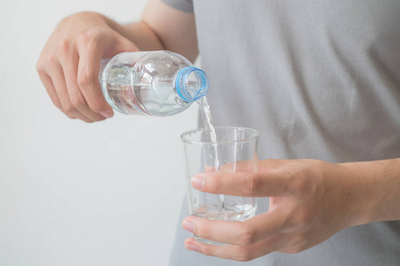 男人手里拿着一瓶水，把水倒进玻璃杯里。