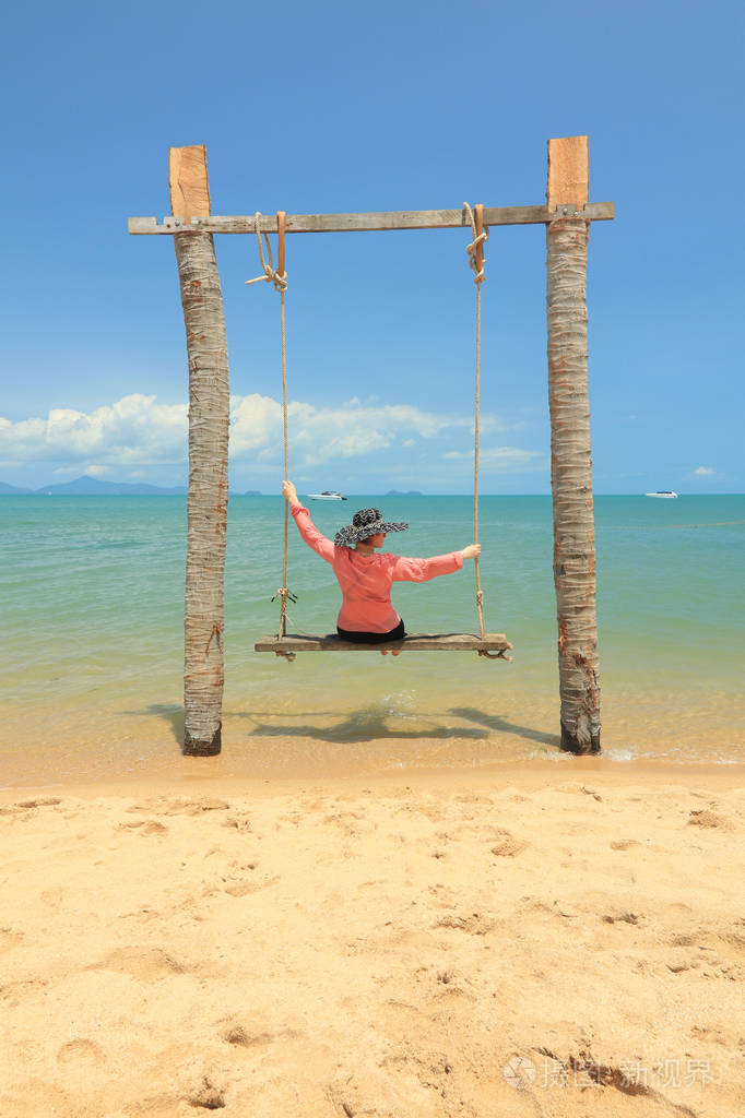 女人坐在沙滩上荡秋千,背景是阳光明媚的海景.