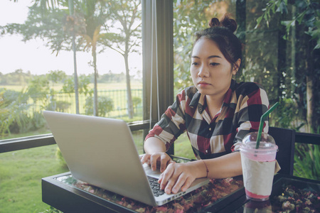 年轻的亚洲女人独自坐在咖啡店里用笔记本电脑工作