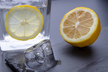 厨房桌子上的玻璃杯里的冷饮。 柠檬和冰加水是夏天凉快的最好方法。 黑暗的背景。