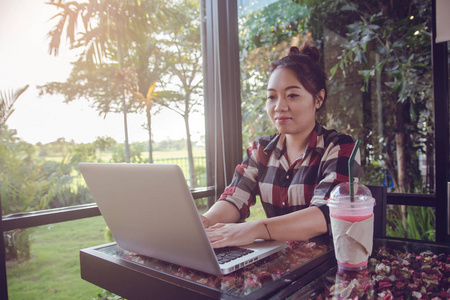 年轻的亚洲女人独自坐在咖啡店里用笔记本电脑工作