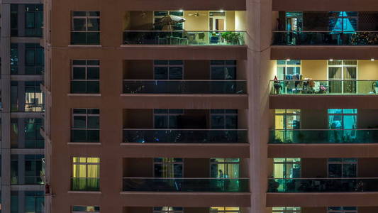 在多层现代玻璃住宅建筑中发光的窗户在夜间时间推移时亮起。 公寓里的人。 摩天大楼在晚上照明。 迪拜码头阿联酋。